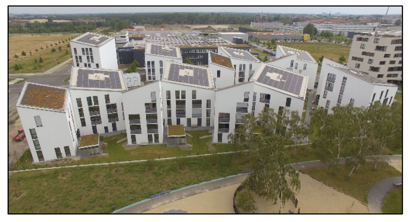 Luftaufnahme eines modernen Gebäudekomplexes mit begrüntem Innenhof und Spielplatz.